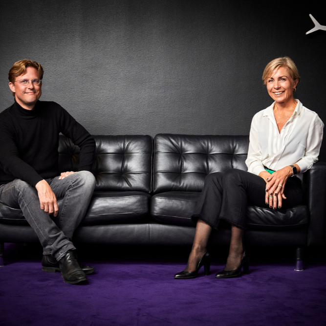 A man and woman sitting on a purple couch.