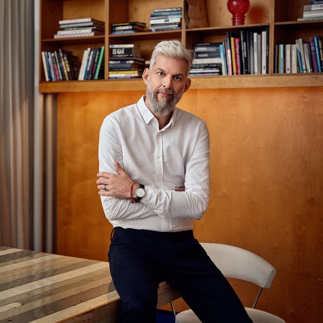 A man sitting at a table with a bookcase in front of him.