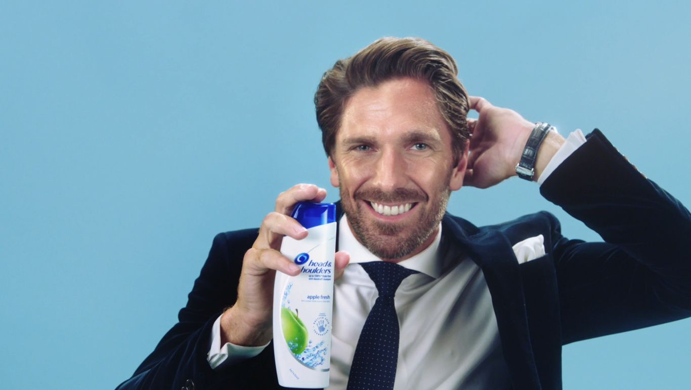 A man in a suit is holding a bottle of shampoo.